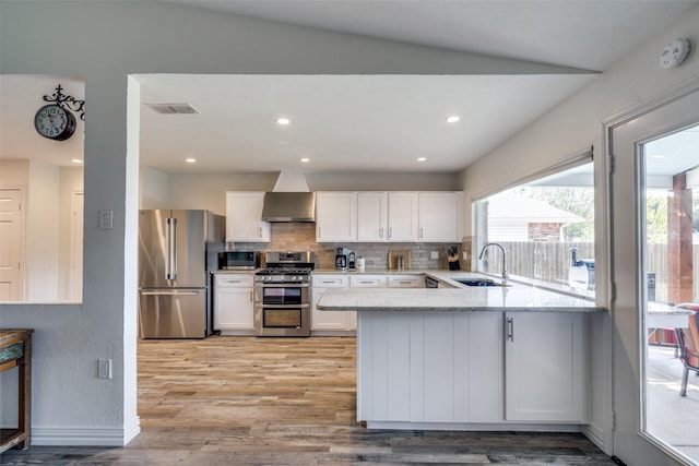 kitchen with wall chimney range hood, stainless steel appliances, white cabinetry, and sink