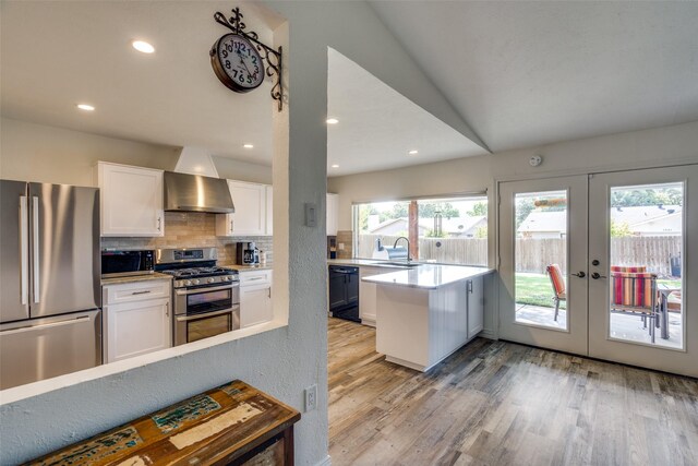 kitchen with french doors, wall chimney exhaust hood, stainless steel appliances, sink, and white cabinetry