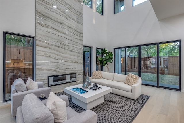 living room with light hardwood / wood-style floors, a premium fireplace, and a high ceiling