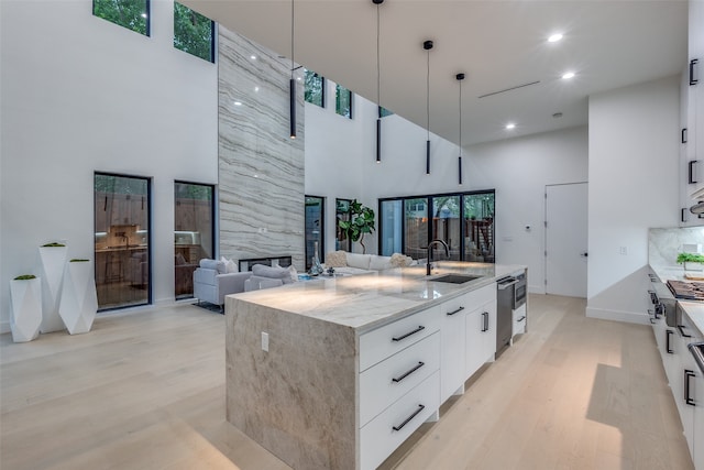 kitchen featuring white cabinets, sink, a high ceiling, a center island with sink, and decorative light fixtures