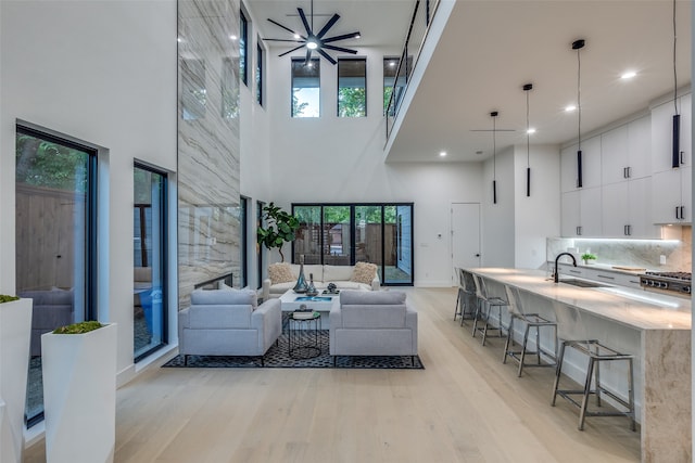 living room featuring light wood-type flooring, a towering ceiling, sink, and plenty of natural light