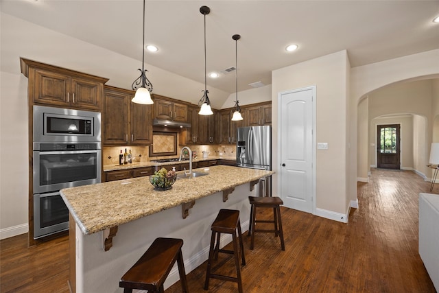 kitchen featuring stainless steel appliances, an island with sink, pendant lighting, and a kitchen bar