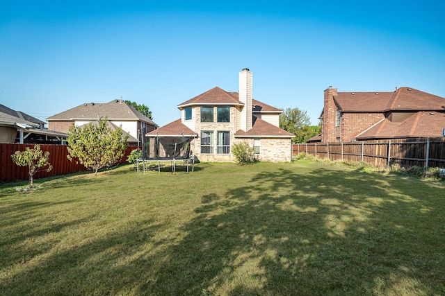 back of house with a trampoline and a lawn