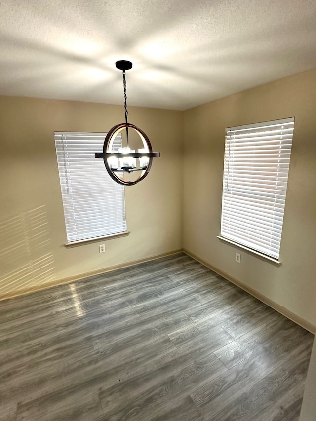 spare room featuring dark wood-type flooring, an inviting chandelier, and a textured ceiling