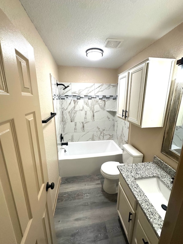 full bathroom with vanity, tiled shower / bath, hardwood / wood-style flooring, and toilet