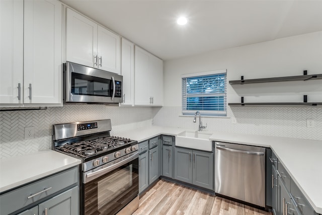 kitchen featuring appliances with stainless steel finishes, white cabinetry, sink, and light hardwood / wood-style flooring