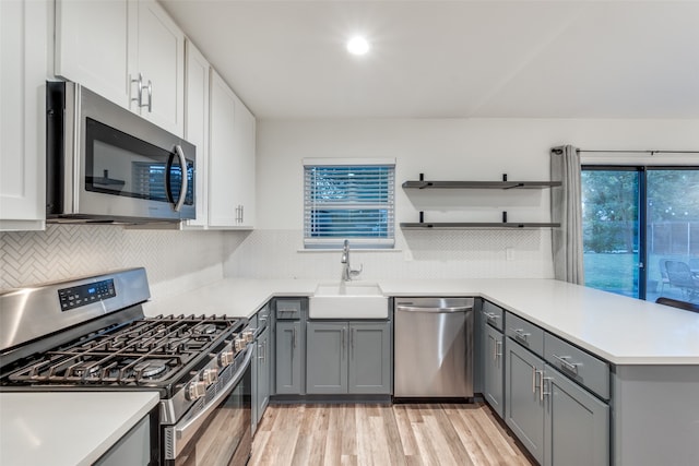 kitchen featuring gray cabinets, light wood-type flooring, sink, decorative backsplash, and appliances with stainless steel finishes