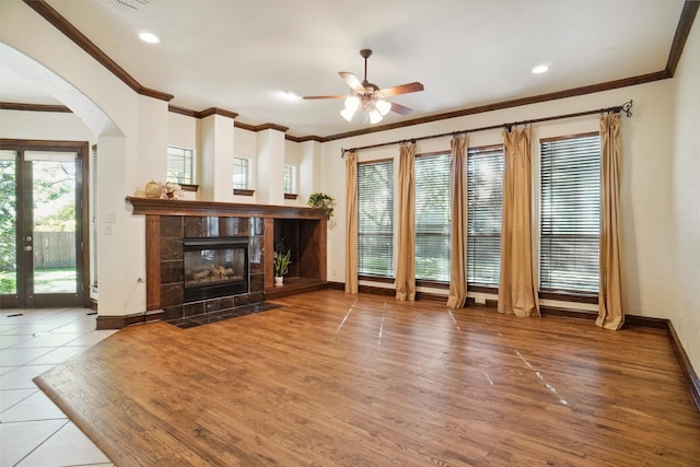 unfurnished living room with a tiled fireplace, ceiling fan, hardwood / wood-style floors, and crown molding