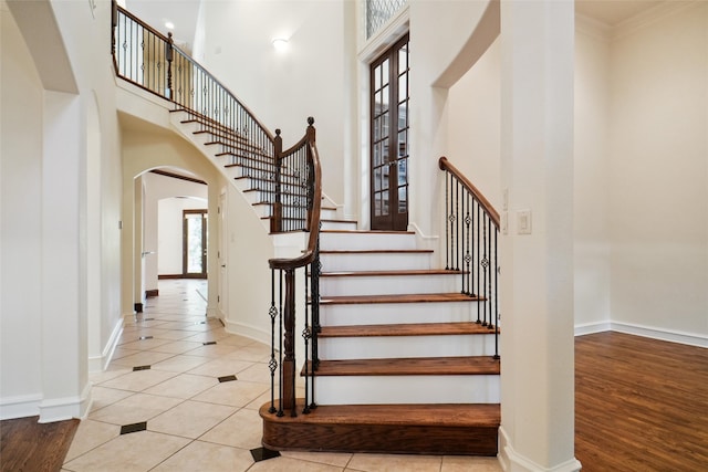 staircase featuring hardwood / wood-style floors, plenty of natural light, a towering ceiling, and crown molding