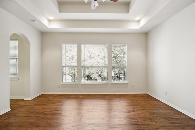 unfurnished room with a tray ceiling, dark hardwood / wood-style floors, and ceiling fan