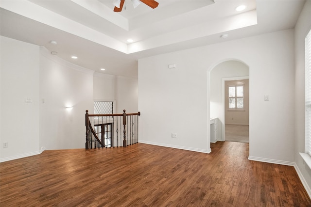 empty room with a tray ceiling, ceiling fan, and dark hardwood / wood-style flooring