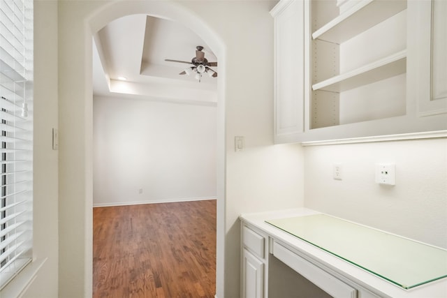 interior space featuring hardwood / wood-style flooring, ceiling fan, white cabinets, and a tray ceiling