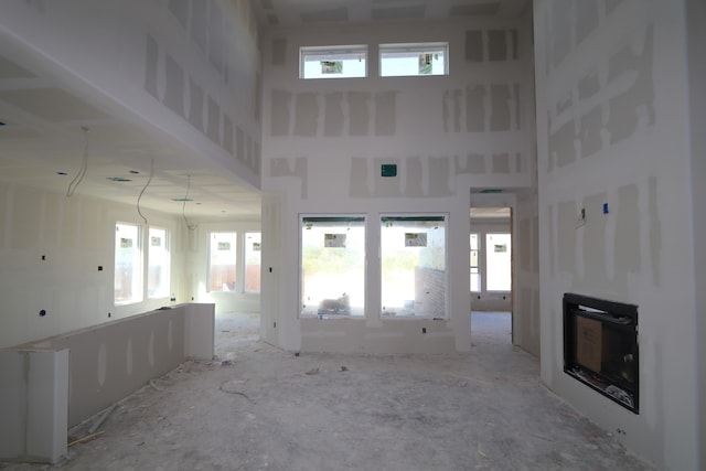 unfurnished living room featuring a towering ceiling, a fireplace, heating unit, and plenty of natural light