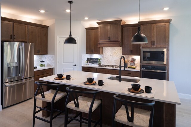 kitchen with a breakfast bar area, appliances with stainless steel finishes, an island with sink, light hardwood / wood-style flooring, and sink