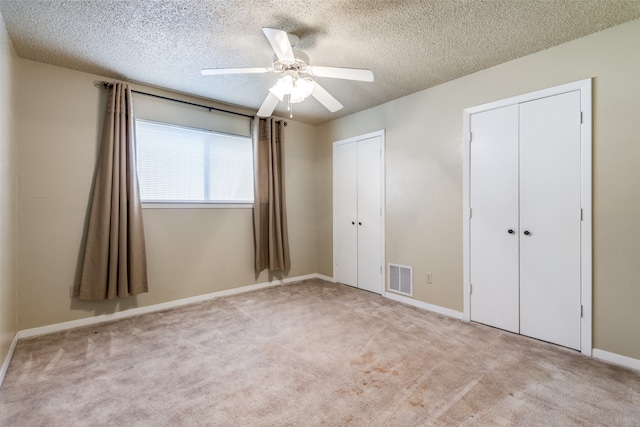 unfurnished bedroom with a textured ceiling, multiple closets, light carpet, and ceiling fan