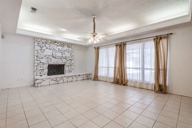 unfurnished living room with a large fireplace, ceiling fan, a tray ceiling, and light tile patterned floors