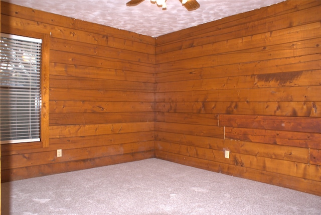 carpeted empty room with ceiling fan and wood walls