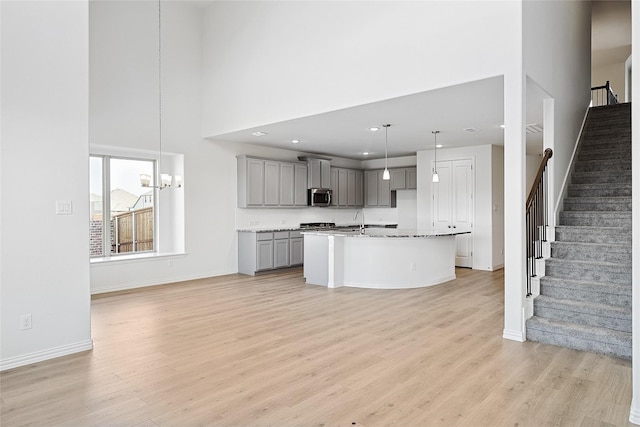 kitchen with sink, hanging light fixtures, light hardwood / wood-style flooring, gray cabinets, and a kitchen island with sink