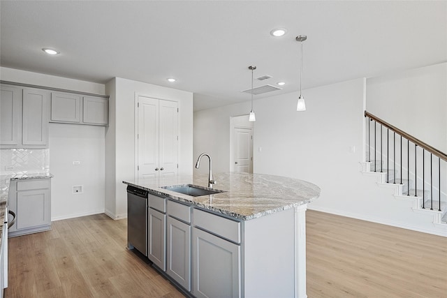 kitchen with sink, stainless steel dishwasher, gray cabinets, an island with sink, and light stone counters