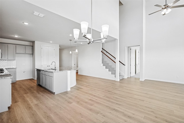 kitchen featuring gray cabinetry, a center island with sink, sink, hanging light fixtures, and light stone counters