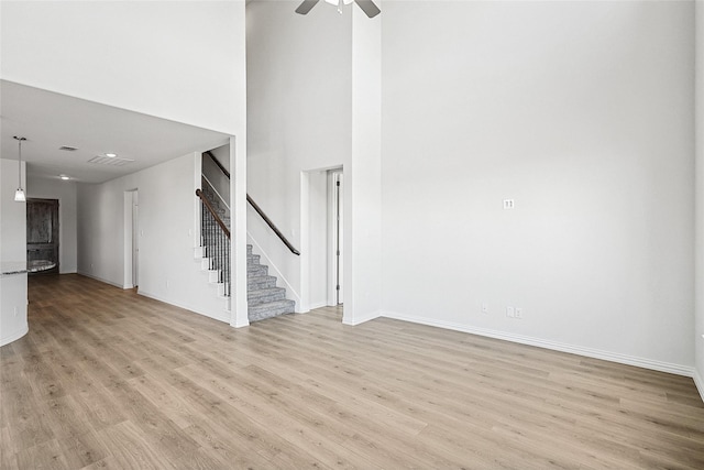 unfurnished living room featuring ceiling fan, light hardwood / wood-style floors, and a high ceiling