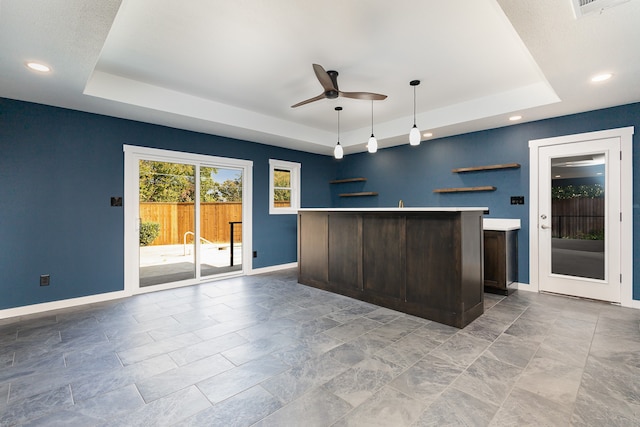 kitchen featuring ceiling fan, a kitchen island, a tray ceiling, and decorative light fixtures