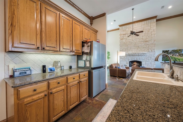 kitchen with dark stone countertops, sink, a fireplace, stainless steel refrigerator, and ceiling fan