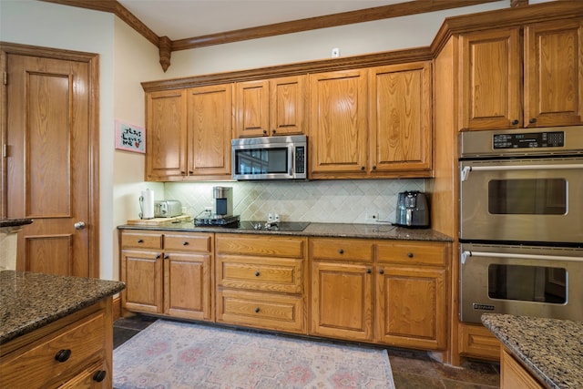 kitchen with appliances with stainless steel finishes, dark tile patterned floors, dark stone countertops, crown molding, and decorative backsplash