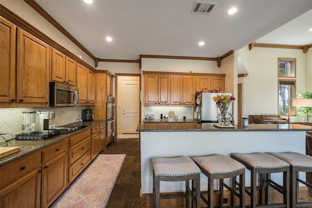 kitchen with ornamental molding, dark stone countertops, stainless steel appliances, and a center island with sink