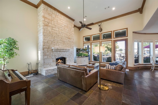 living room with a high ceiling, a stone fireplace, crown molding, and ceiling fan