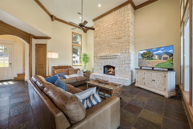 living room featuring ornamental molding, a stone fireplace, a towering ceiling, and ceiling fan