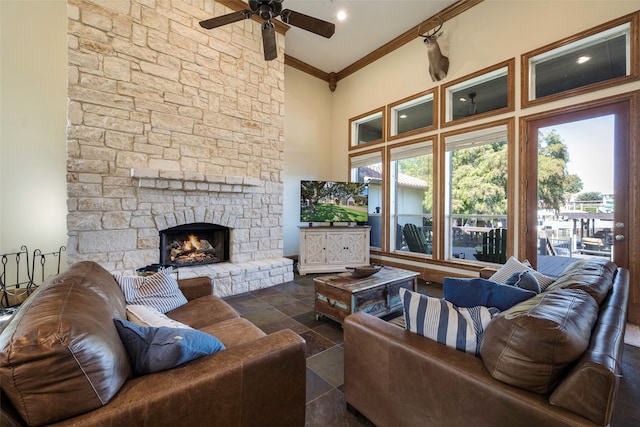 living room with ceiling fan, a stone fireplace, a towering ceiling, and ornamental molding