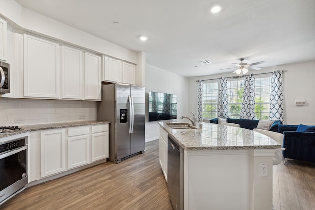 kitchen featuring tasteful backsplash, wood-type flooring, a kitchen island with sink, white cabinetry, and stainless steel appliances