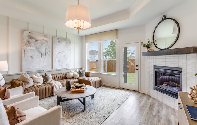 living room featuring a raised ceiling, a fireplace, light hardwood / wood-style flooring, and ornamental molding