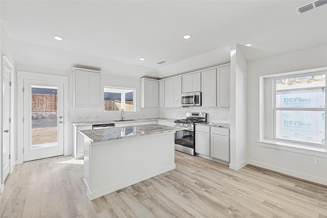 kitchen featuring sink, appliances with stainless steel finishes, light stone countertops, white cabinets, and a kitchen island