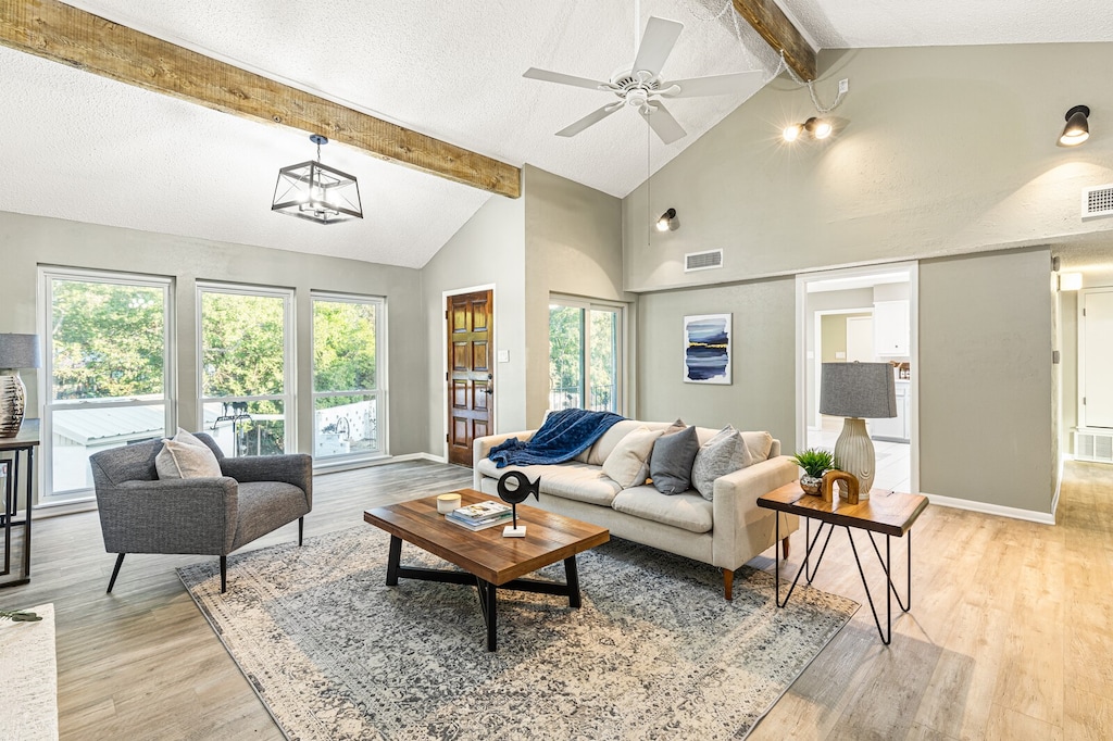 living room with ceiling fan, beam ceiling, light hardwood / wood-style flooring, high vaulted ceiling, and a textured ceiling