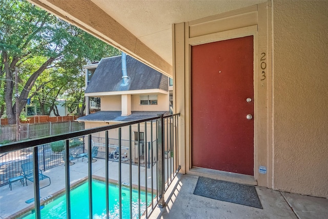 property entrance featuring fence, a fenced in pool, stucco siding, and a balcony