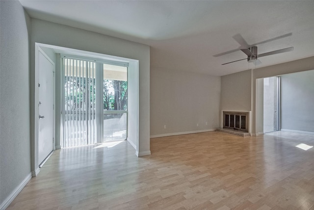 unfurnished living room with a glass covered fireplace, light wood-style floors, baseboards, and a ceiling fan