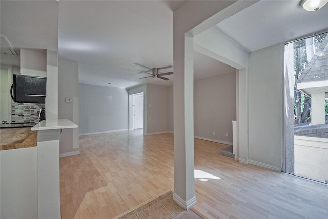 unfurnished living room with light wood finished floors, baseboards, and ceiling fan