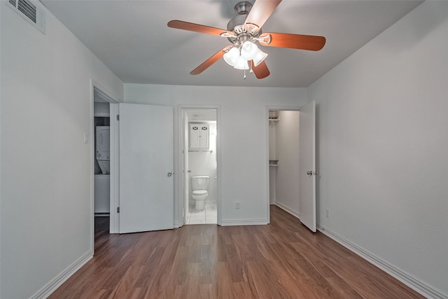 unfurnished bedroom featuring stacked washer / drying machine, ensuite bathroom, light wood-type flooring, and ceiling fan