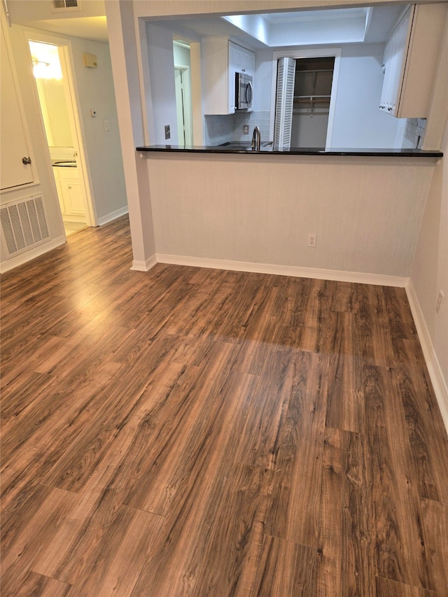 kitchen featuring wood-type flooring, backsplash, kitchen peninsula, and white cabinetry