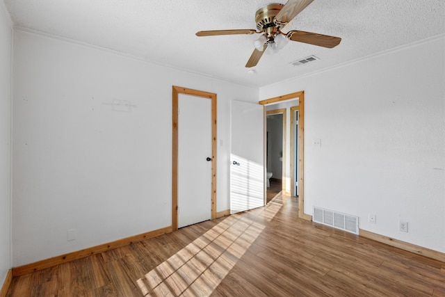 empty room featuring ceiling fan, hardwood / wood-style flooring, ornamental molding, and a textured ceiling