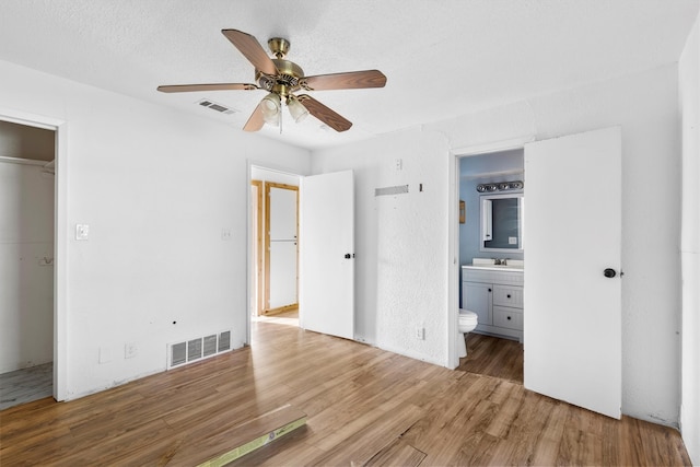 unfurnished bedroom featuring ceiling fan, a closet, wood-type flooring, connected bathroom, and a textured ceiling