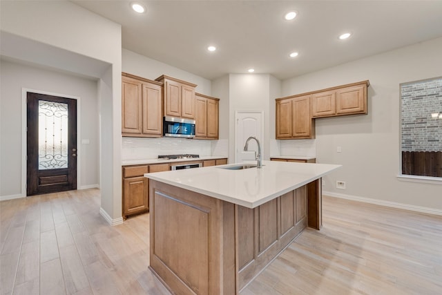 kitchen featuring backsplash, stainless steel appliances, sink, a center island with sink, and light hardwood / wood-style floors