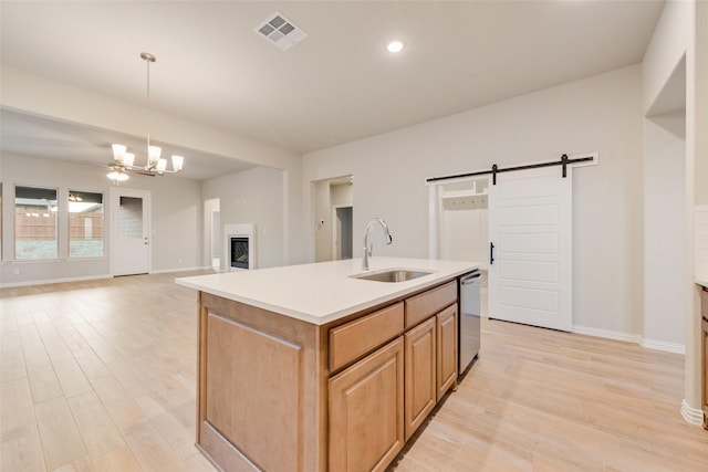 kitchen with dishwasher, sink, a barn door, pendant lighting, and a center island with sink