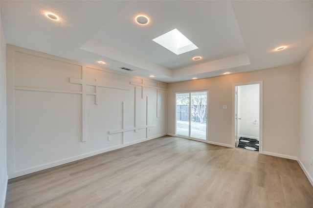 empty room with light hardwood / wood-style flooring, a raised ceiling, and a skylight