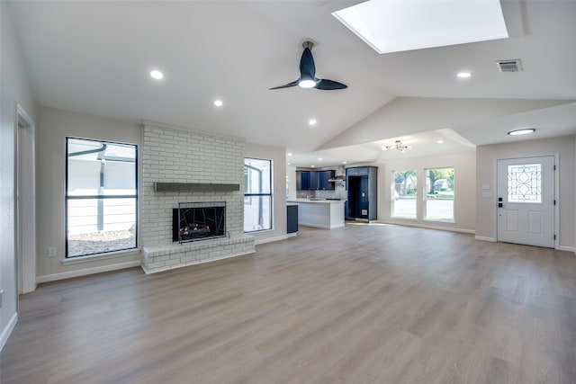 unfurnished living room featuring lofted ceiling with skylight, a fireplace, light hardwood / wood-style floors, and ceiling fan