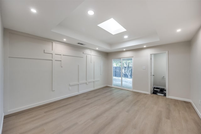 spare room with a tray ceiling, a skylight, and light hardwood / wood-style floors