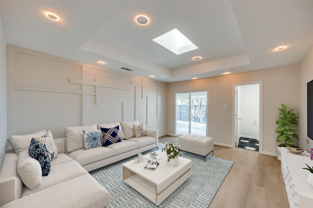 living room featuring a tray ceiling, a skylight, and hardwood / wood-style floors