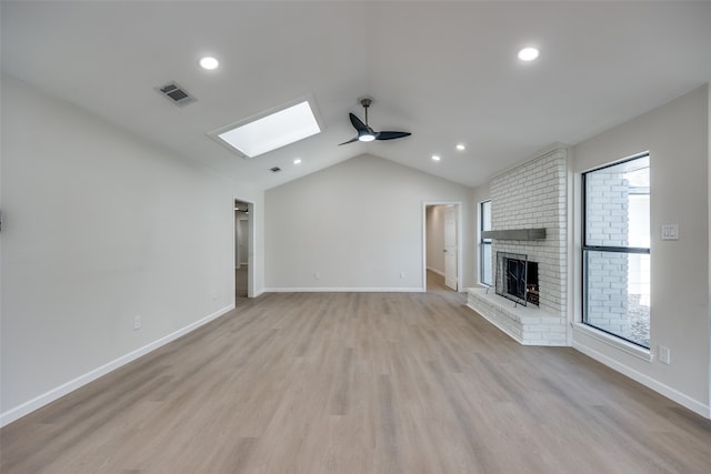 unfurnished living room with lofted ceiling with skylight, light hardwood / wood-style flooring, a brick fireplace, and ceiling fan